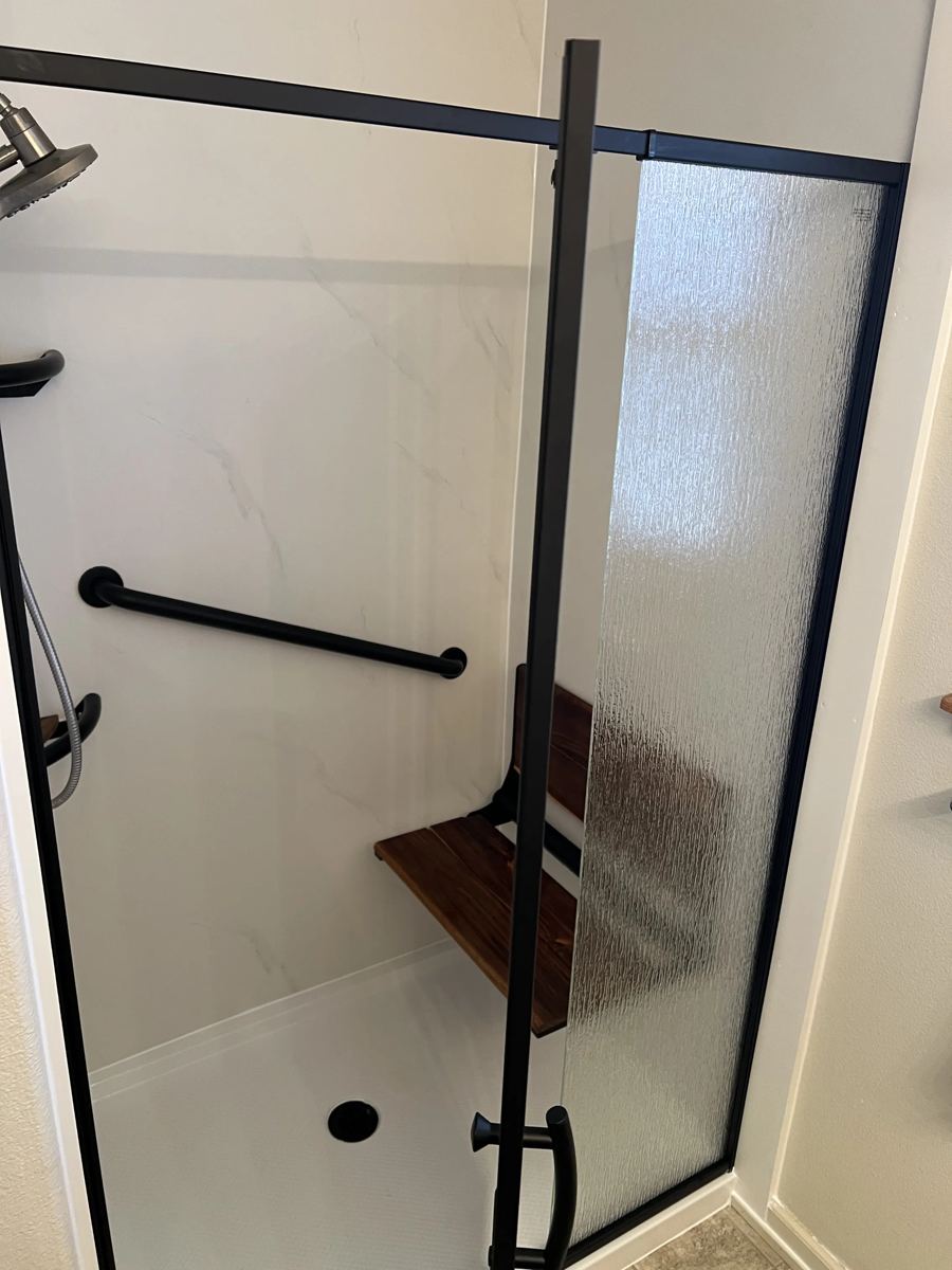Finished shower with glass enclosure, grab bars, and teak bench
